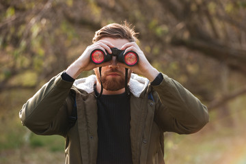 Poster - Bearded man looking at field-glass standing in the forest.