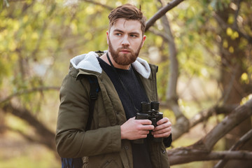 Wall Mural - Serious bearded man holding field-glass standing in the forest