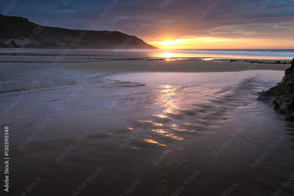 Sunrise over a beach stream at Caswell Bay, one of the most popular and ...