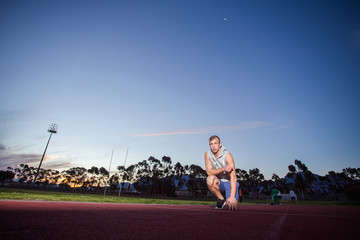 Male sprinter athlete on a tartan athletic track getting ready f