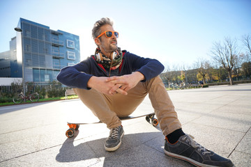 Wall Mural - Trendy urban guy sitting on skateboard in park