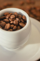 Sticker - Coffee beans on white coffee cup over the wooden table.