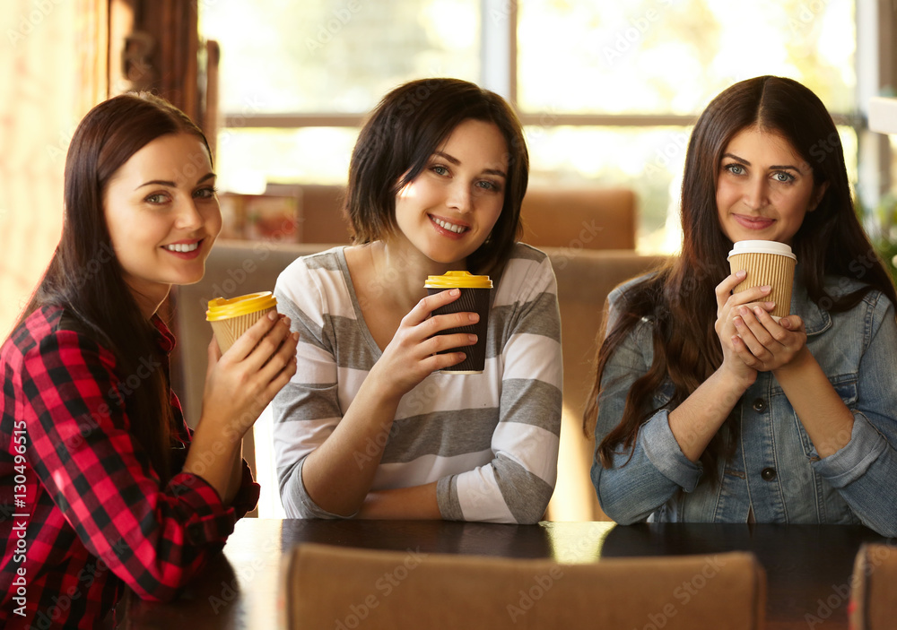 Cheerful young women drinking coffee in cafe on sunny day