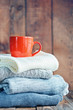 Sweaters Closeup, Stack of knitted winter clothes with red cup on wooden background. Toning image