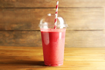 Wall Mural - Delicious strawberry milkshake in plastic cup on wooden background