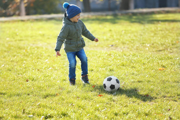 Wall Mural - Cute little boy playing football on soccer pitch