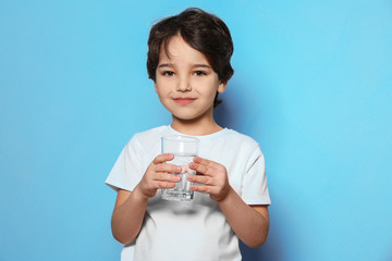 Cute little boy drinking water from glass on blue background