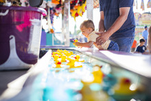 Father Lifting Son Playing With Rubber Ducks Floating In Water At Amusement Park