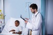 © WavebreakMediaMicro - Doctor looking at report while patient sleeping on bed