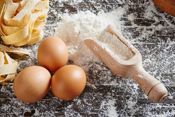 Wooden spoon with flour, egg and pasta on floured wooden table