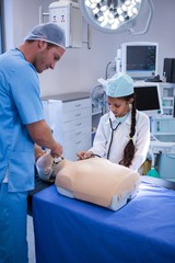Poster - Doctor assisting girl in examining on dummy with stethoscope