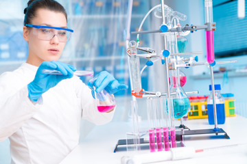 Canvas Print - Attractive young female scientist working in laboratory.  Woman scientist looking at a red test tube in a lab. Young woman in chemical lab