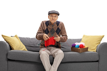 Poster - Confused elderly man sitting on a sofa and knitting