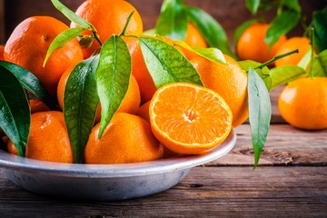 Wall Mural - Juicy ripe tangerines with leaves in a bowl on wooden background.