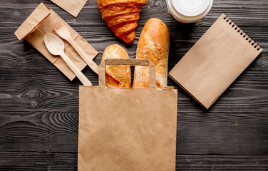 Wall Mural - cup coffee and bread in paper bag on wooden background