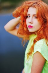 Portrait of an adorable brown-eyed girl with her hand up, combing gorgeous bright red hair.