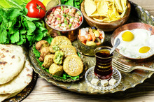 Arabic Cuisine,Egyptian Breakfast Of Fried Egg, Plate Of Flafel,beans,pickles,chips, Fresh Organic Vegetables,traditional Backing Bread And Cup Of Tea In Copper Tray..