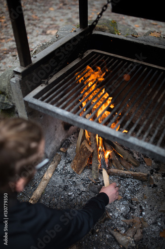 Young Man Setting A Fire In An Outdoor Fireplace Preparing