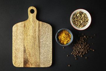 Cutting board with bowls with tumeric, cardamom on black backgro