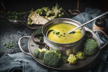 Cooking pot with green romanesco and broccoli soup and ladle on dark rustic kitchen table . Healthy food and diet nutrition concept.