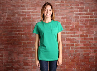 Wall Mural - Young woman in blank green t-shirt standing against brick wall