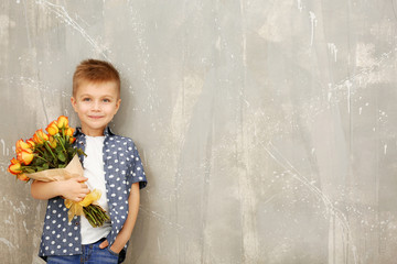 Cute boy with bouquet of beautiful flowers near grunge wall