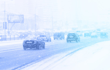 Aufkleber - A lot of many cars on the highway in winter in the city in snowfall or blizzard, snow flakes falling, soft focus, light background toned blue. Concept slippery dangerous road.
