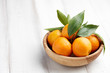Fresh ripe tangerines with leaves in a wooden bowl on white wooden background