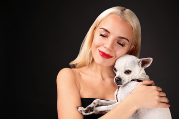 Wall Mural - Beautiful girl holding cute dog on dark background