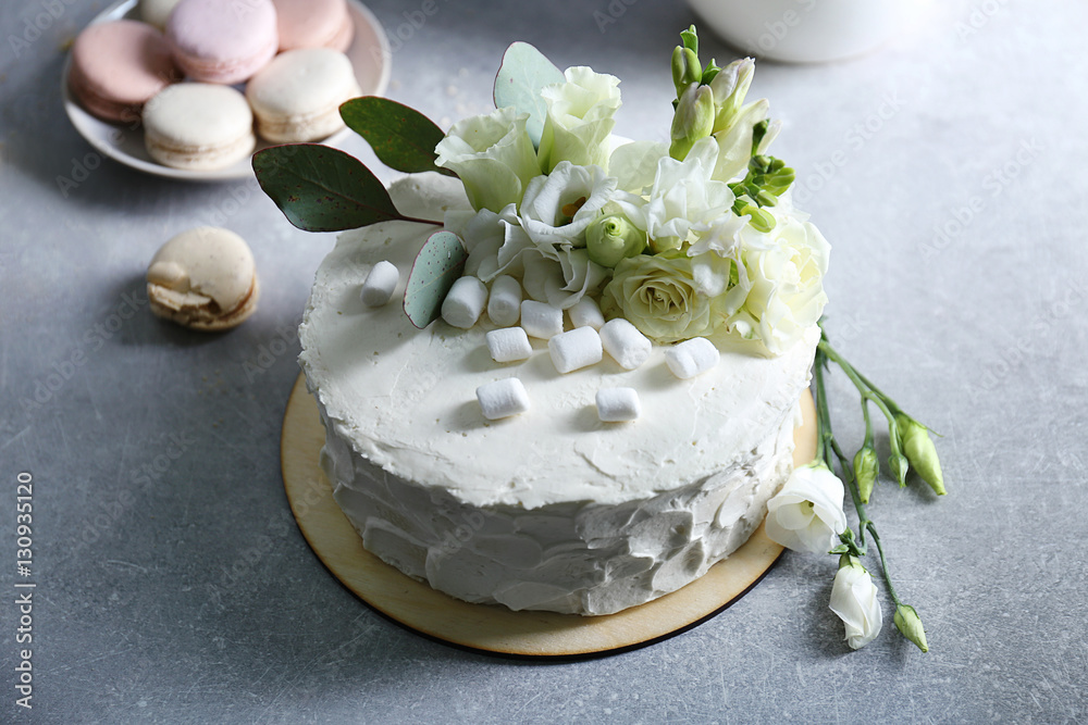 Delicious cake decorated with marshmallows and flowers on table