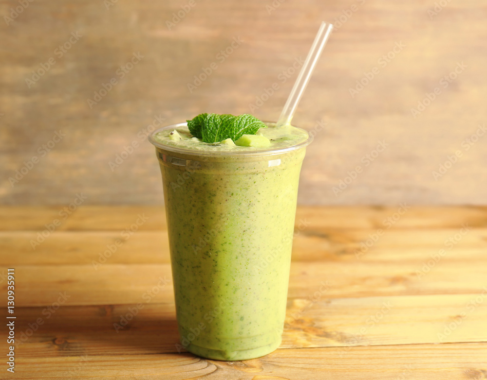 Delicious kiwi milkshake in plastic cup on wooden background
