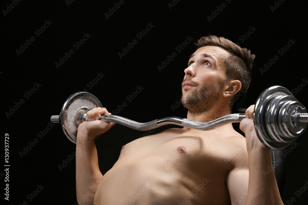 Sporty man doing exercises with barbell on black background