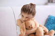 Funny little girl with cuddly toy sitting on sofa at home