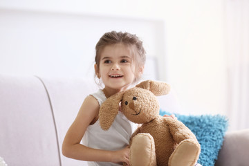 Wall Mural - Funny little girl with cuddly toy sitting on sofa at home