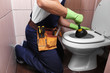 Plumber repairing toilet with hand plunger, closeup