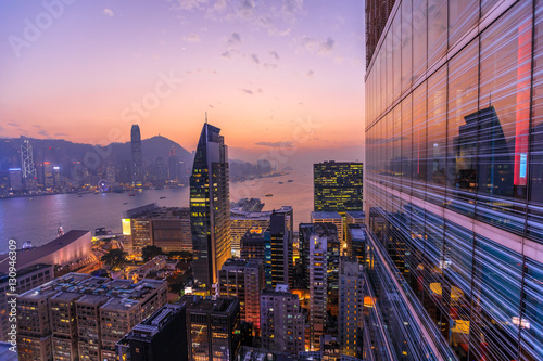 Obraz Dibond Spektakularny widok z lotu ptaka na Victoria Harbour, wieżowce i panoramę Hongkongu w nocy. Skyline odzwierciedlenie w szklanej fasadzie nowoczesnego budynku.