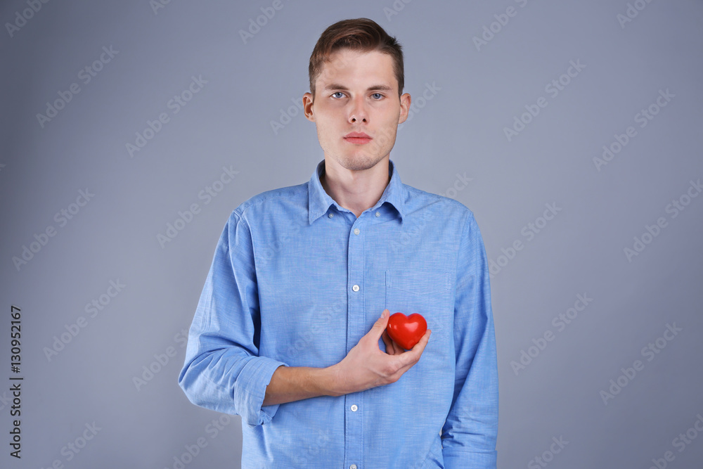 Handsome young man holding red heart on color background