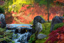 Small Waterfall Over Rocks At The Edge Of A Pond With Autumn Reflections In Water