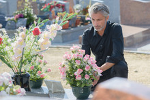 Man Putting Flowers On Tomb