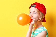 Funny Teenager Girl In Red Hat Inflating Balloon On Yellow Background