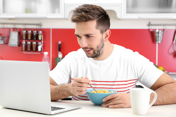 Sticker - Young man having breakfast while working with laptop in kitchen