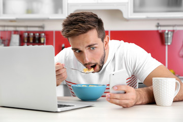 Sticker - Young man having breakfast while working with laptop in kitchen