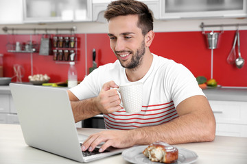 Sticker - Young man having snack while working with laptop in kitchen