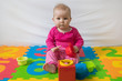 © Ivica Drusany - Cute bare feet  baby girl in pink clothes sitting on colorful puzzle play mat and playing with toys.