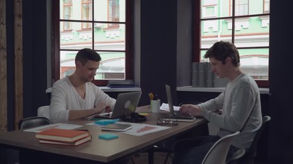 Aufkleber - Happy business team using laptop in the modern office. Smiling man talking with colleagues at work. Handsome professional men wearing in casual clothes like jeans and pullover. Businessman typing on