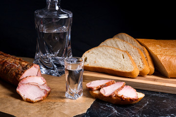 Bottle and shot glass with vodka with slices of smoked meat on b