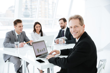 Wall Mural - Photo of elderly business man by the table with colleagues