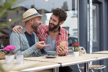 Gay couple sat sharing content on phone outside a cafe