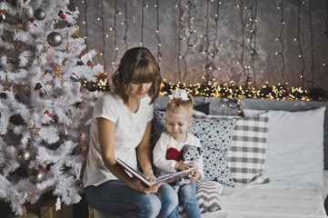 Little girl with mother reading a book sitting under the Christm