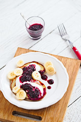 Wall Mural - Paleo pancakes with banana, coconut, yogurt and bluberry jam on a white plate with red fork. Bright healthy breakfast. White wooden table